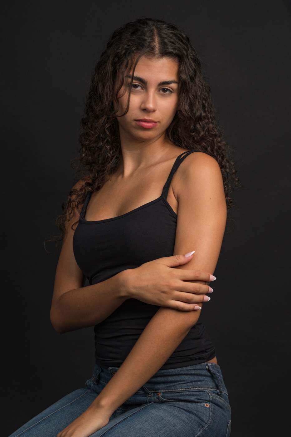 Vitoria sentada con los brazos cruzados, top negro, fondo negro