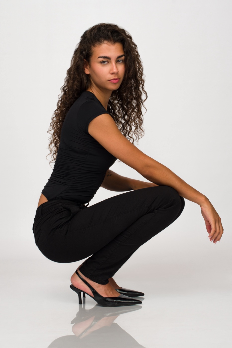 Vitoria en cuclillas con body negro, pantalón negro y tacón